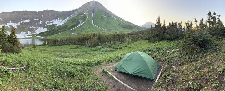 Panorama of the alpine meadow near Windfall Lake with a green peak, the lake, and the tent