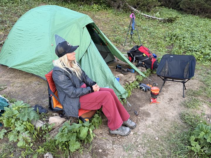 Stacie in a camp chair beside the tent and stove at Windfall Lake