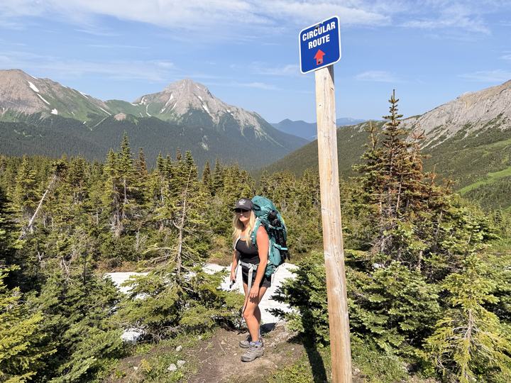 Stacie beside a Circular Route sign post above the trees near Windfall Lake