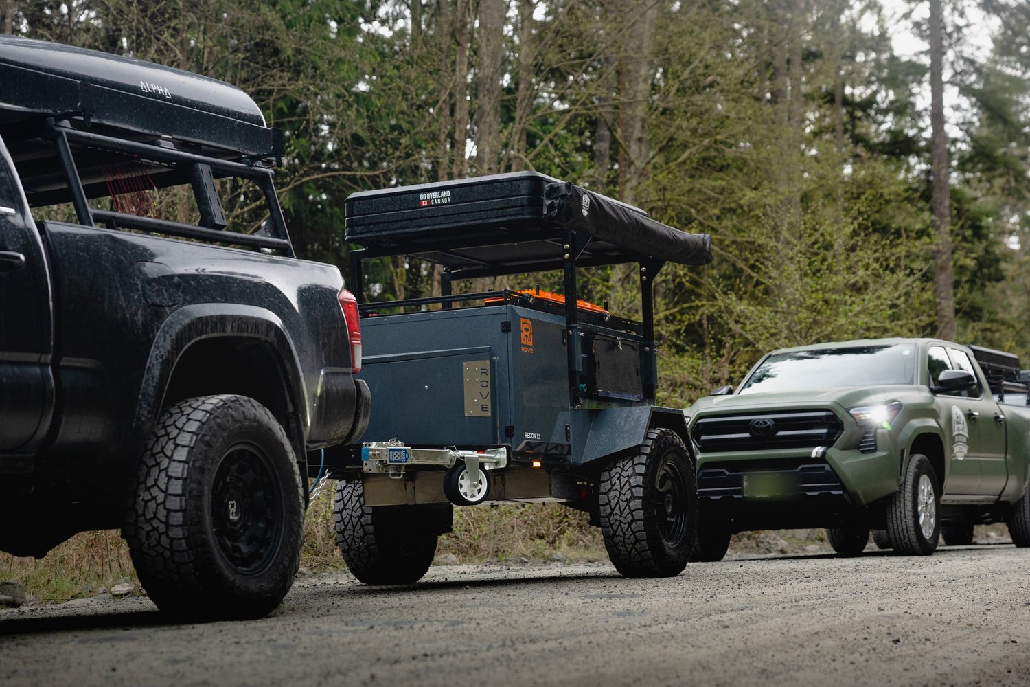 A Rove Recon parked between two overland trucks on a forest road