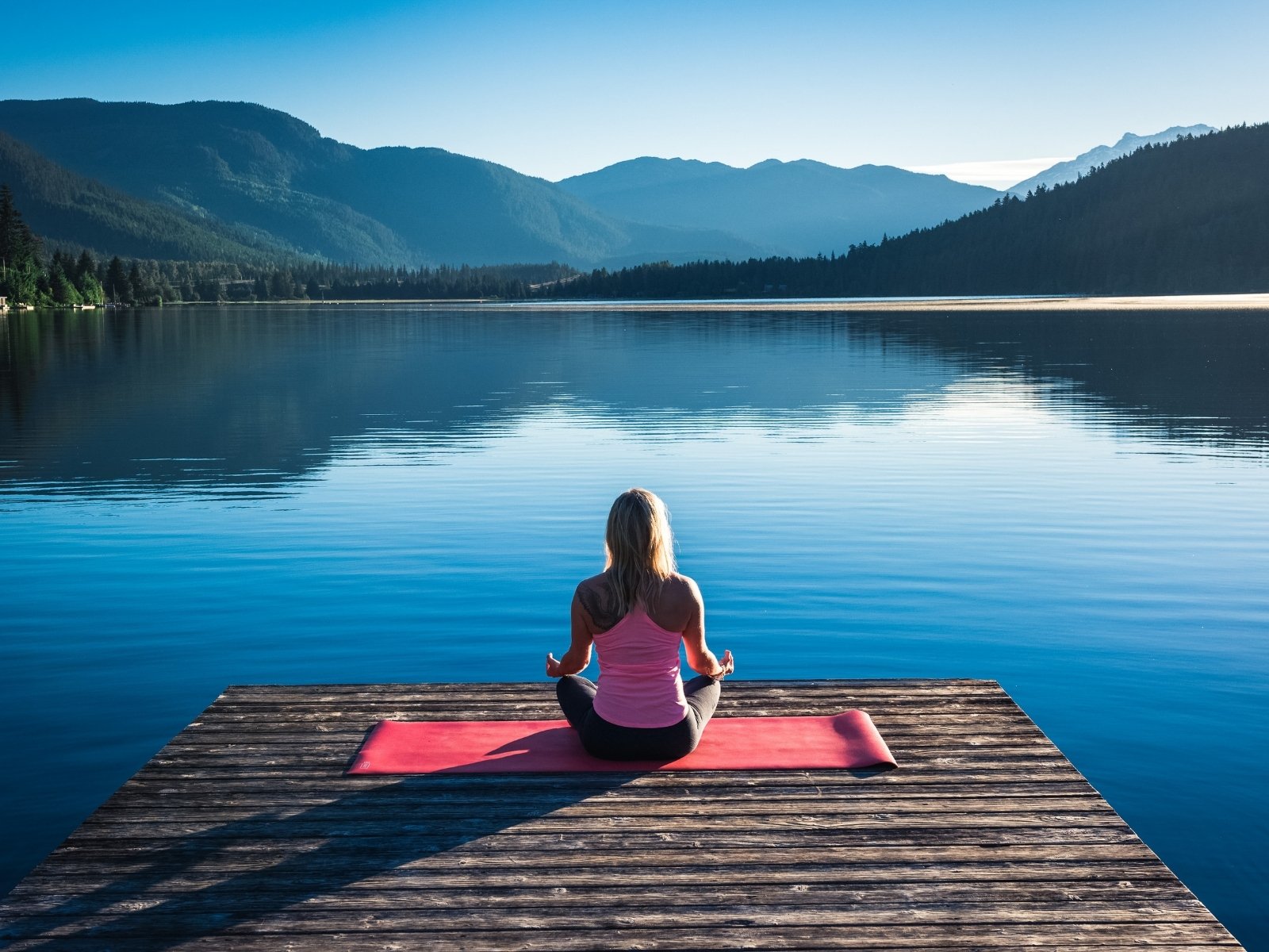 Stacie seated in meditation on a dock at a still mountain lake