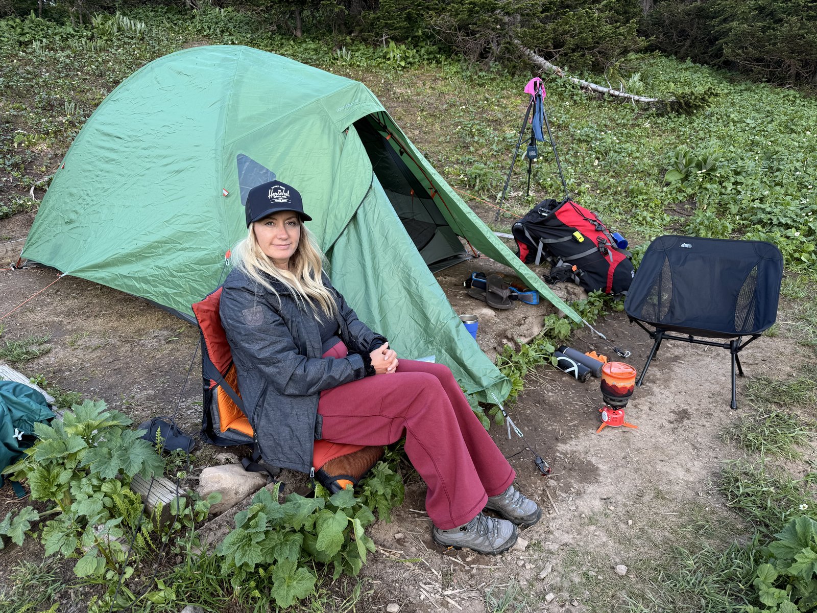 Stacie sitting with a hot drink beside her tent at an alpine camp