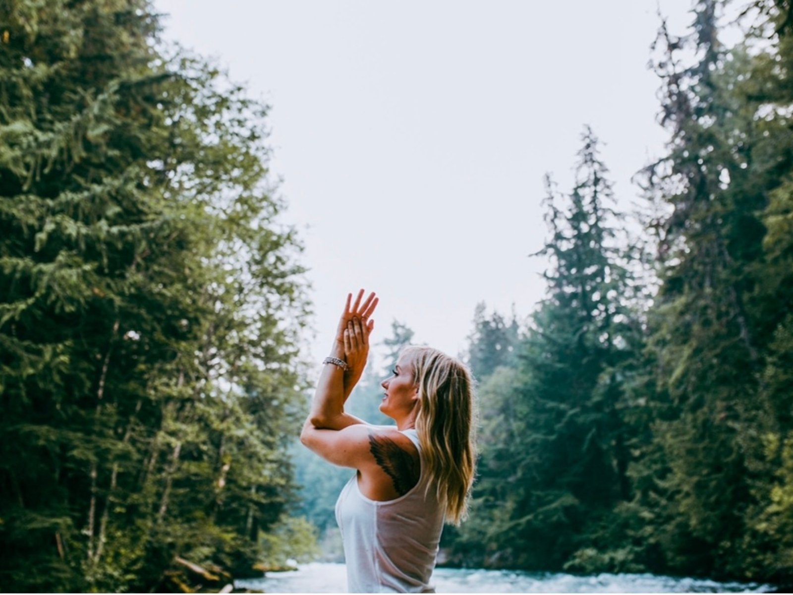 Stacie moving through a yoga practice beside a river, tall evergreens behind her