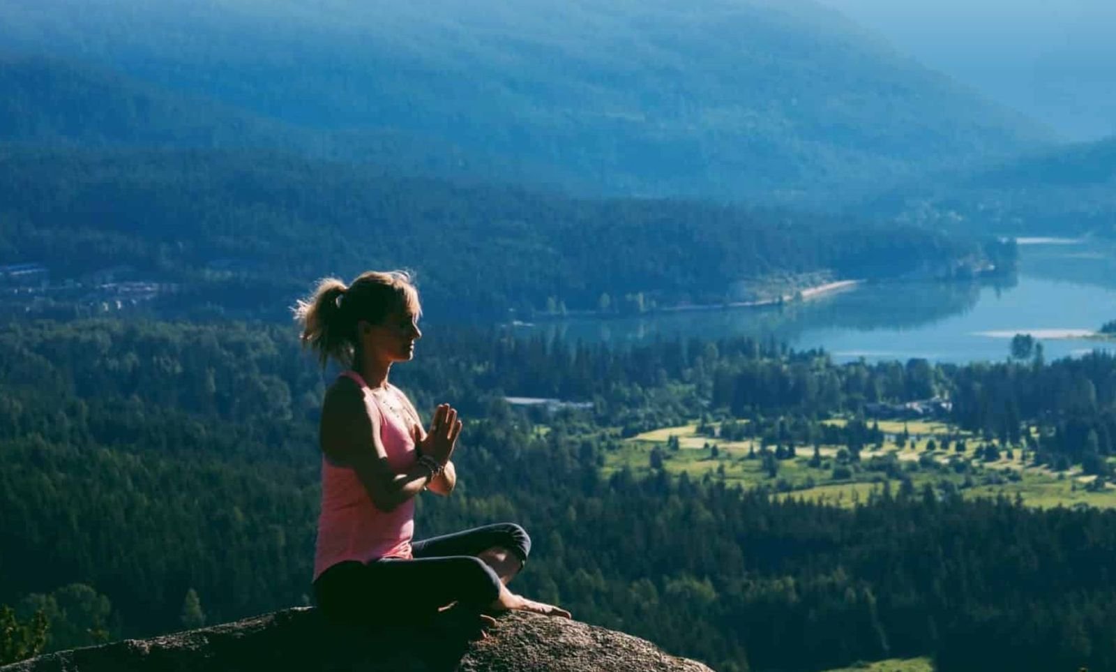 Stacie sitting in meditation on a bluff above a mountain lake at sunrise