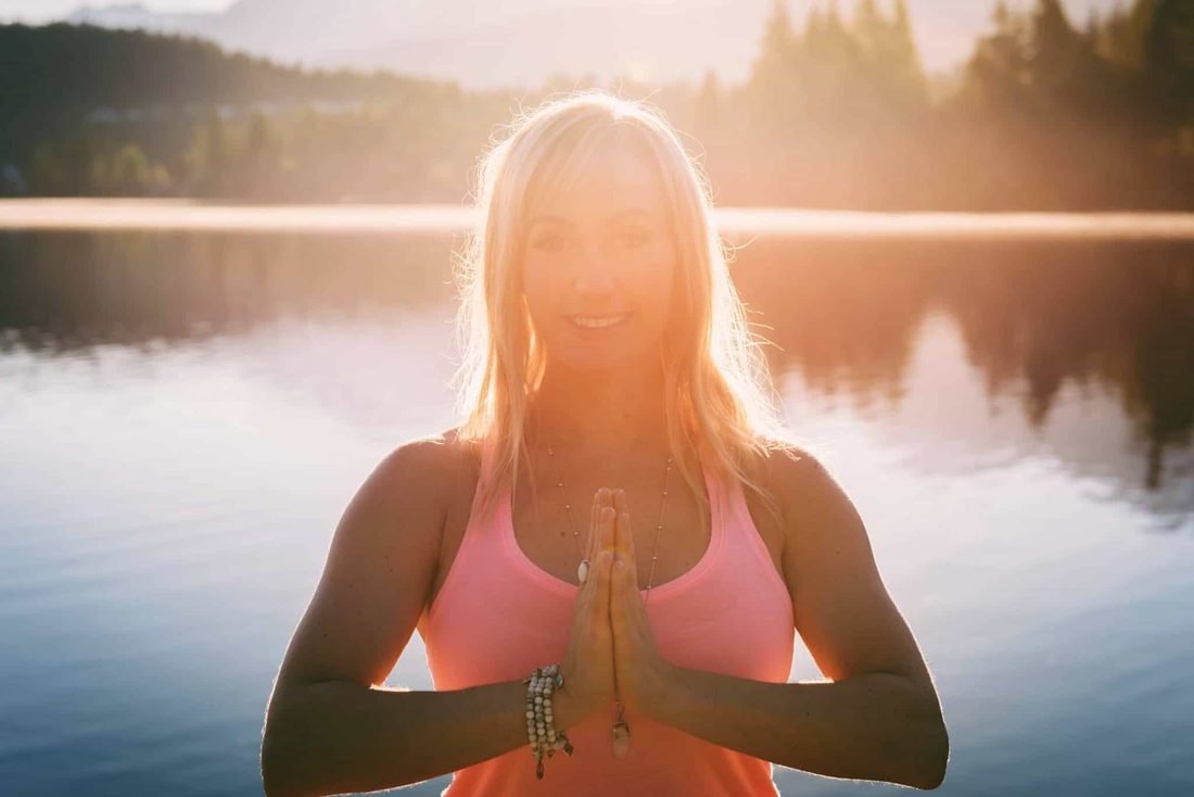 Stacie at sunrise by a mountain lake, hands together at her heart